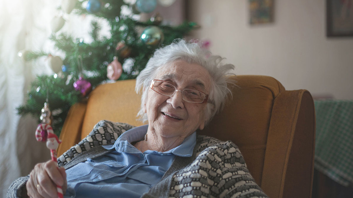 Happy elderly woman sat in chair near Christmas tree