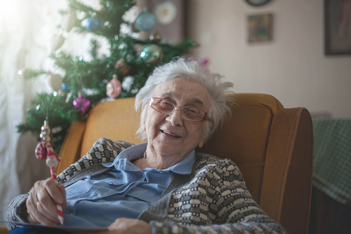 Happy elderly woman sat in chair near Christmas tree