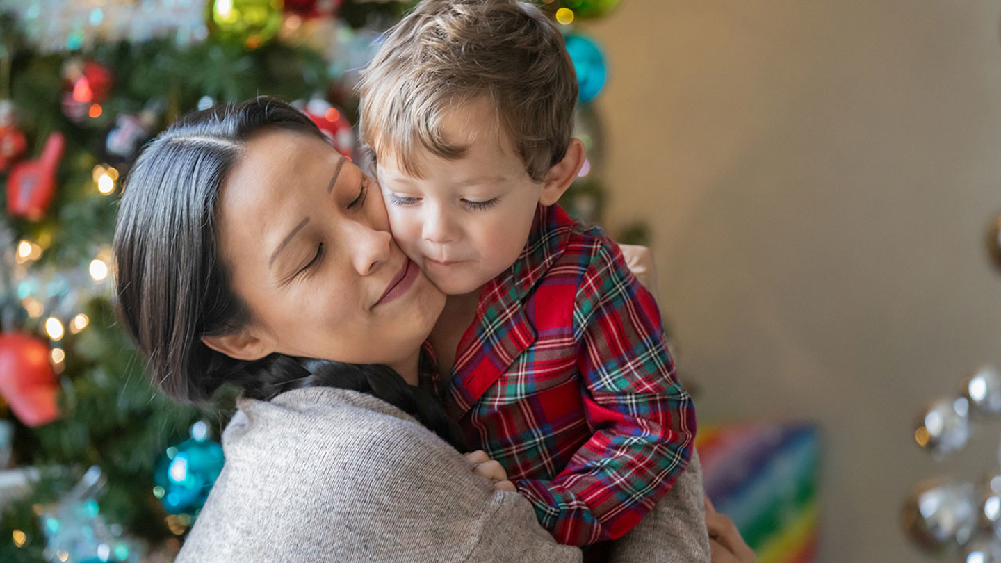 Mother and child hugging in front of Christmas tree