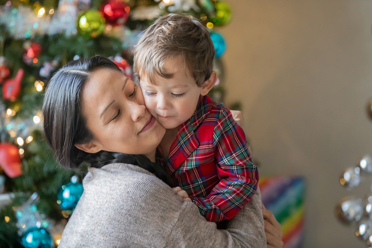 Mother and child hugging in front of Christmas tree